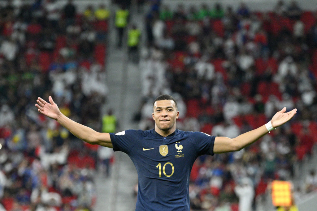 Kylian Mbappé celebrating with open arms in a match while wearing the French national team jersey.