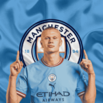 Erling Haaland's wearing a Manchester City jersey, standing in front of the club’s logo with both hands pointing upwards.