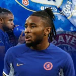 A graphic featuring Christopher Nkunku in a Chelsea FC jersey with a blue background. Nkunku appears in the foreground with a focused expression, and a secondary image of him blowing up a blue balloon is in the background. The design includes elements of the Chelsea and Bayern Munich logos